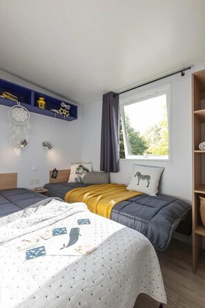 A bedroom with two beds, a window with a view, a shelf with decorative items, and a dreamcatcher.