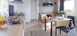 A compact kitchen with a stove, sink, and various kitchen items. There is a dining area with a table and chairs, and a sofa with cushions. A window provides natural light.