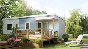 A mobile home with a wooden deck, surrounded by potted plants and a grassy lawn. - ZEcamping 3* avec piscine chauffée club enfant animations pet friendly (Erquy)