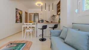 Ein modernes Wohnzimmer mit einer Couch, einem Couchtisch und einem Essbereich mit Stühlen. Im Hintergrund ist eine Küche zu sehen.