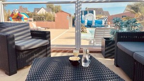 A patio area with wicker furniture, a table with a drink and a bottle, and a view of a swimming pool and inflatable slides.