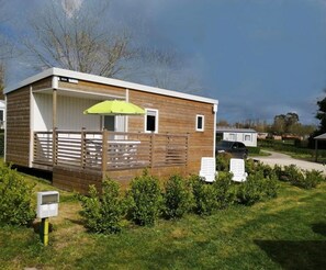 A mobile home with a wooden exterior, a covered porch, and a green umbrella.