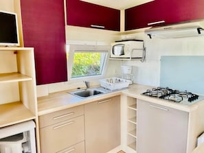 A compact kitchen with a gas stove, microwave, sink, and a window providing natural light.