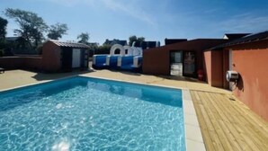 A swimming pool with a wooden deck, a small building with a door, and a blue and white structure in the background.