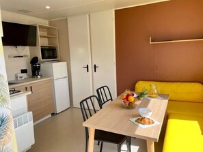 Une cuisine compacte équipée d’un four à micro-ondes, d’une machine à café et d’un petit réfrigérateur. On y trouve une table à manger avec des chaises et un canapé jaune.