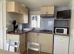 Una cucina compatta con mobili in legno, un piano cottura a gas, un forno a microonde e un televisore.