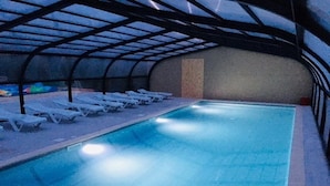 An indoor swimming pool with clear water, surrounded by white lounge chairs and a covered roof structure. - ZEcamping 3* animé piscine couverte chiens acceptés locatif TV 30m2 (Erquy)