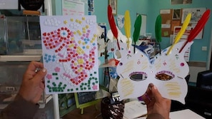 Une personne tenant une œuvre d’art en mosaïque aux couleurs vives et un objet d’artisanat en papier qui ressemble à un oiseau.