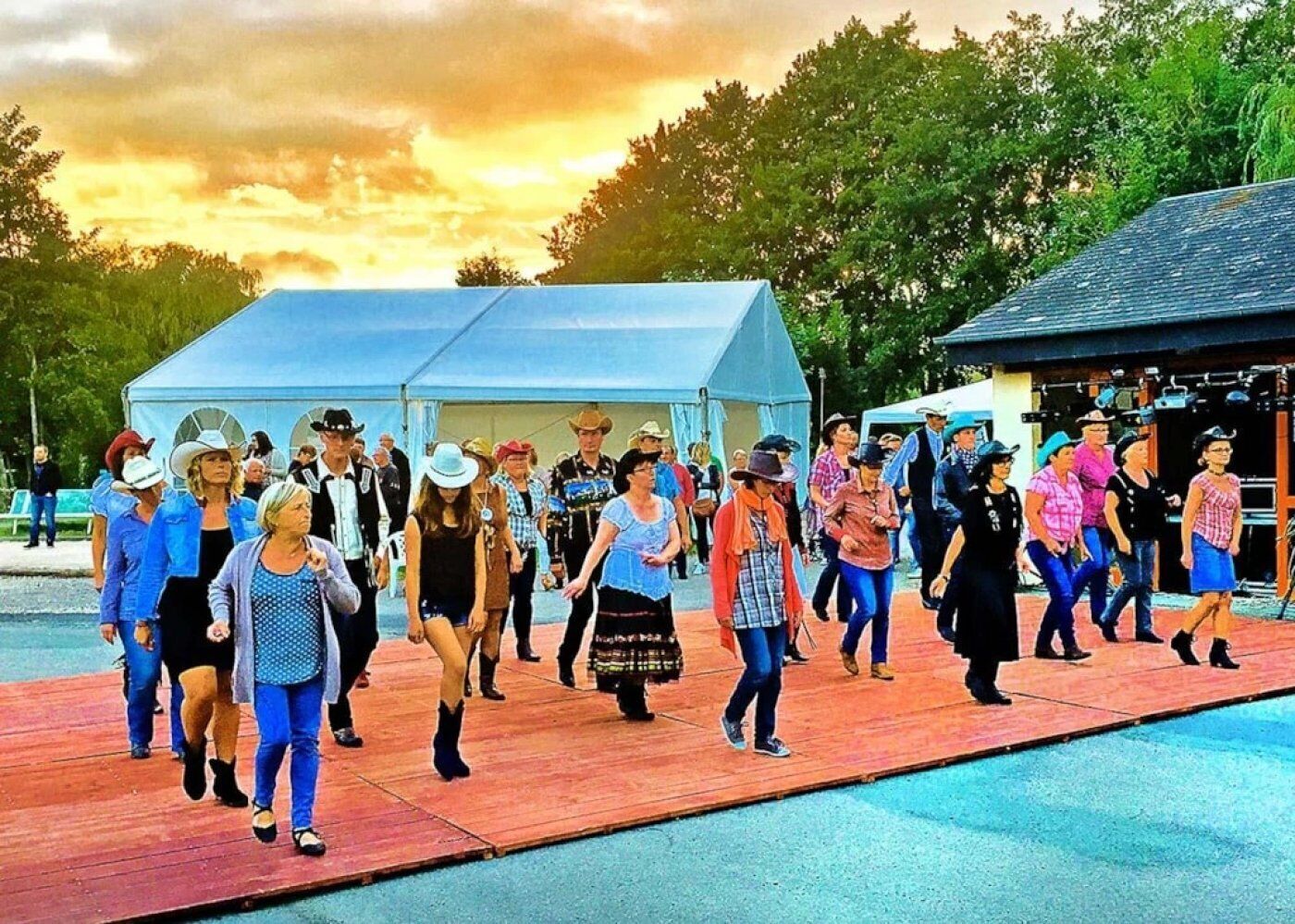 Un gruppo di persone che cammina su una passerella di legno in un parco, con una tenda blu e un edificio sullo sfondo.