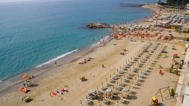 A beach with rows of sun loungers and umbrellas, a pier extending into the sea, and a rocky outcrop in the water. - ZEcamping 2* pataugeoire pet friendly fitness cabane 24m2 4 pers (Pietra Ligure)