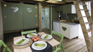 A wooden dining area with a table set for four, green chairs, and a heart-shaped cabinet with a kitchen in the background. - ZEcamping 2* pataugeoire pet friendly fitness cabane 24m2 4 pers (Pietra Ligure)