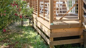 A wooden deck with a railing, a covered area, and a building with a window. - ZEcamping 2* pataugeoire animaux acceptés fitness mobil-home TV clim (Pietra Ligure)