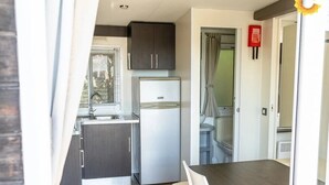 A compact kitchen with a refrigerator, a sink, and cabinets. There is a dining area with a table and chairs. - ZEcamping 2 étoiles pataugeoire fitness mobil-home TV clim 31m2 6 pers (Pietra Ligure)