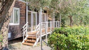 A wooden cabin with a staircase leading to a deck, surrounded by trees and greenery. - ZEcamping 2 étoiles pataugeoire fitness mobil-home TV clim 31m2 6 pers (Pietra Ligure)