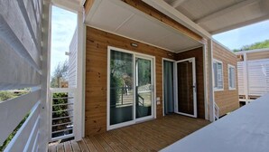 Een overdekt houten terras met schuiframen die uitkomen op een patio.