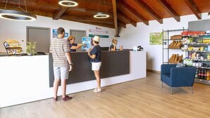 A reception area with a wooden ceiling, a reception desk, a blue chair, and shelves with various items. - ZEcamping 3 étoiles pataugeoire club enfant locatif TV LV clim 90m2 (Le Sauze-du-Lac)
