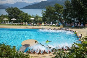 A swimming pool with a view of a lake and mountains, surrounded by lounge chairs and umbrellas. - ZEcamping 3 étoiles pataugeoire club enfant locatif TV LV clim 90m2 (Le Sauze-du-Lac)