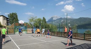 Una cancha de baloncesto al aire libre con jugadores, una red y montañas al fondo.