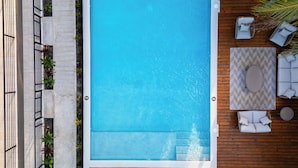 Ein Pool auf dem Dach mit Liegestühlen, einer Holzterrasse und Blick auf die umliegenden Gebäude.