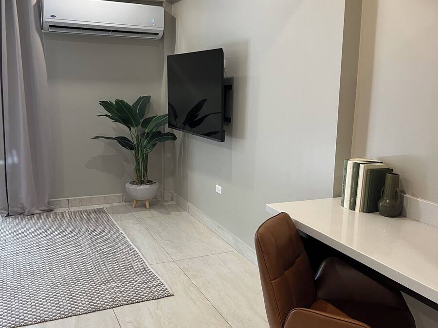 A modern living room with a mounted TV, a potted plant, a brown leather chair, and a white console table with books and a vase.
