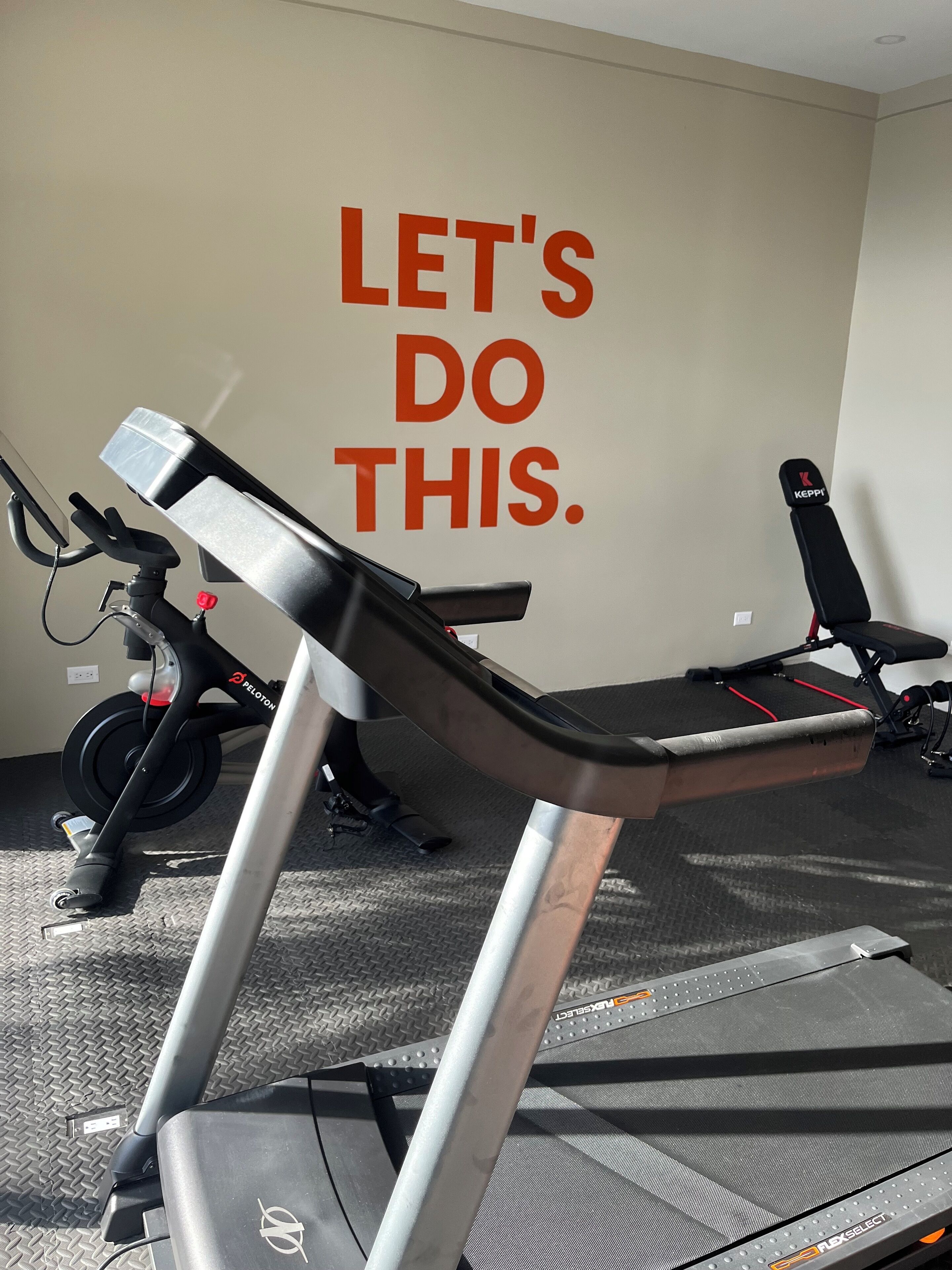 Un gimnasio con cintas de correr, una pared con mensajes motivacionales y un banco.