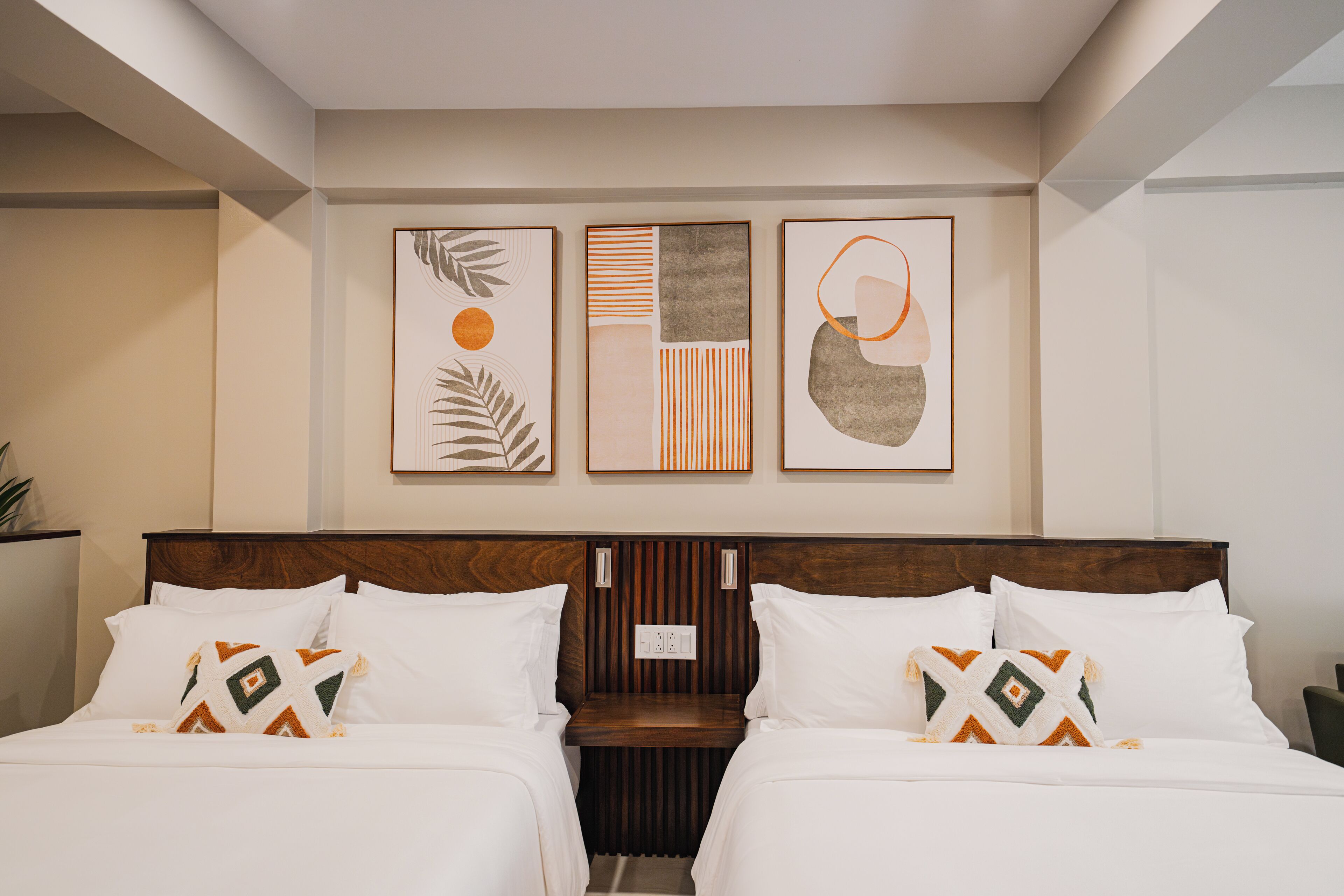 A hotel room with two beds, a wooden headboard, and three framed artworks on the wall.