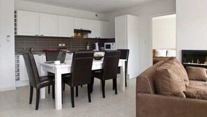 Eine moderne Küche mit weißen Schränken, einem Esstisch mit Stühlen und einem Kamin im Wohnbereich.