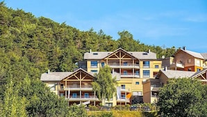 Ein mehrstöckiges Hotel mit Balkonen vor einer dichten Waldlandschaft und blauem Himmel.
