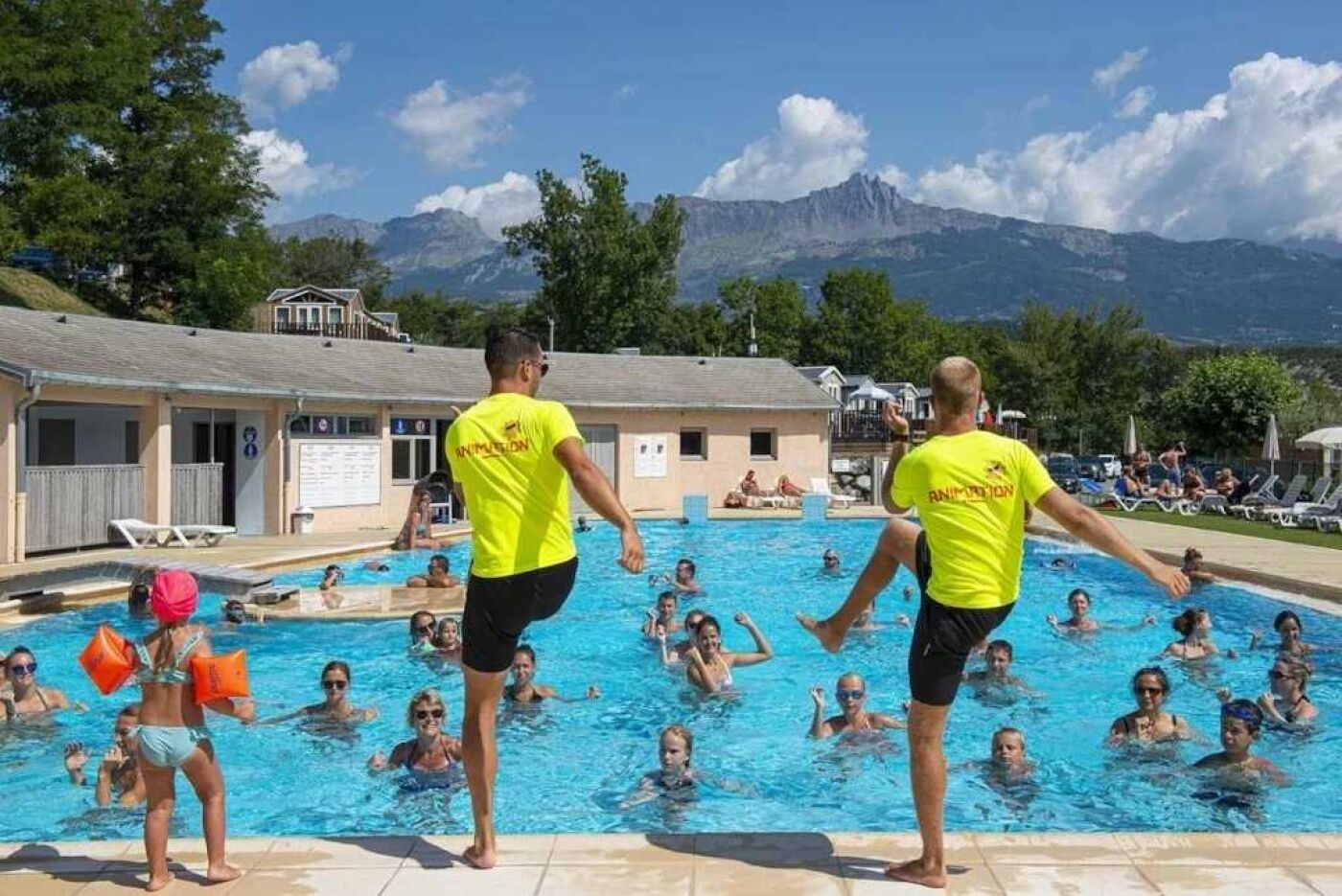 Una piscina amb gent, envoltada de muntanyes i arbres.