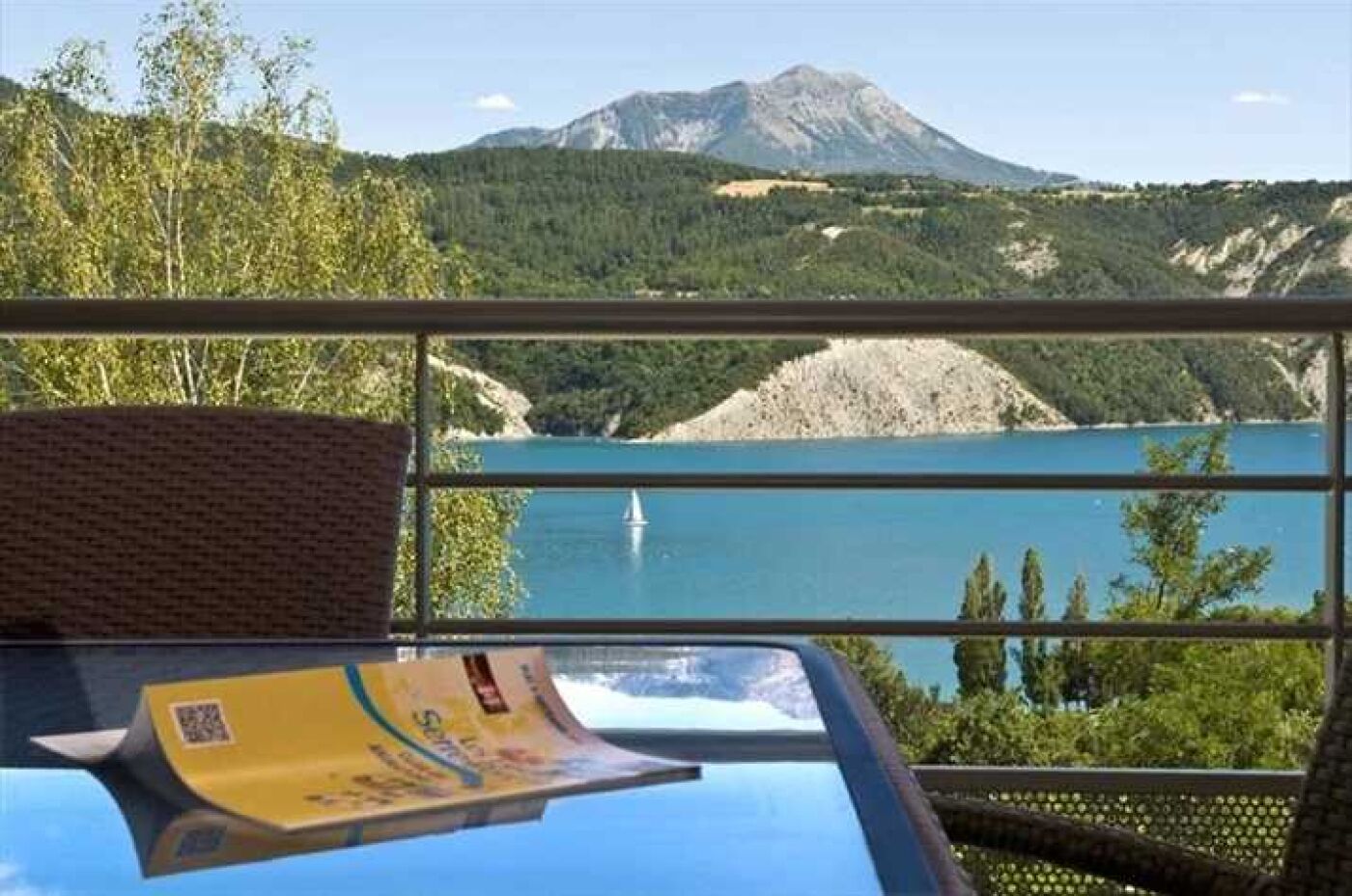 A balcony with a view of a lake, a mountain, and a sailboat.