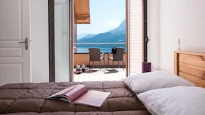 Ein Schlafzimmer mit einem Bett, einem Buch und Blick auf einen Balkon mit Stühlen und einem Tisch.