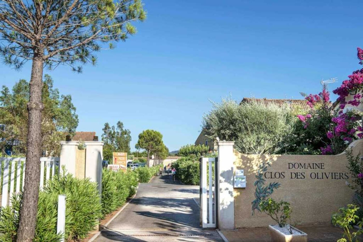 Une entrée fermée par un portail donne accès au domaine Clos Des Oliviers, avec un chemin bien dégagé menant à la propriété.