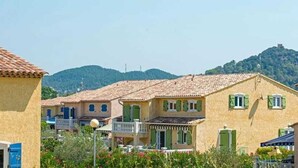 A row of Mediterranean-style buildings with terracotta roofs, a balcony, and a view of a hill in the background.