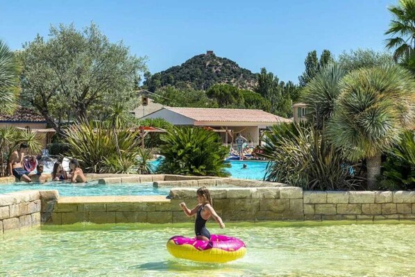 Un espace piscine comprenant plusieurs piscines, entouré de palmiers et avec une colline en arrière-plan.