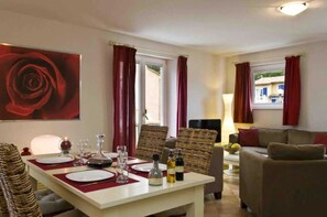 Un coin repas avec une table dressée pour deux personnes, un canapé et un grand tableau représentant une rose rouge accroché au mur.