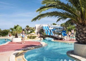 Una piscina con tobogán de agua, palmeras y un puente.