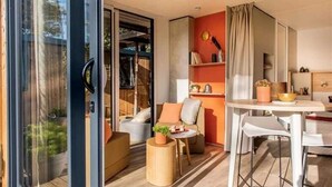 A modern interior with a glass door leading to a balcony, a dining area with a table and chairs, and a seating area with cushions and a small table.