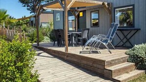 Une terrasse en bois avec des meubles d’extérieur, une pergola et une vue sur une maison.
