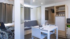Une pièce de taille modeste, équipée d’un fauteuil roulant, d’une petite table avec des verres, d’un canapé et d’une petite cuisine.