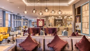 A modern hotel lobby with seating areas, a bar, and a large bookshelf. - Premier Inn London Hammersmith - Talgarth Road (London)