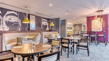 A modern restaurant with round tables, cushioned seating, and a large abstract wall art piece.