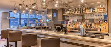 Zona de bar con varios taburetes, una barra y lámparas colgantes.