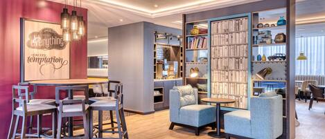 Un interior moderno con una zona de bar, asientos, una estantería y una cocina.