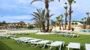Zona de piscina con sillas de descanso blancas y palmeras.