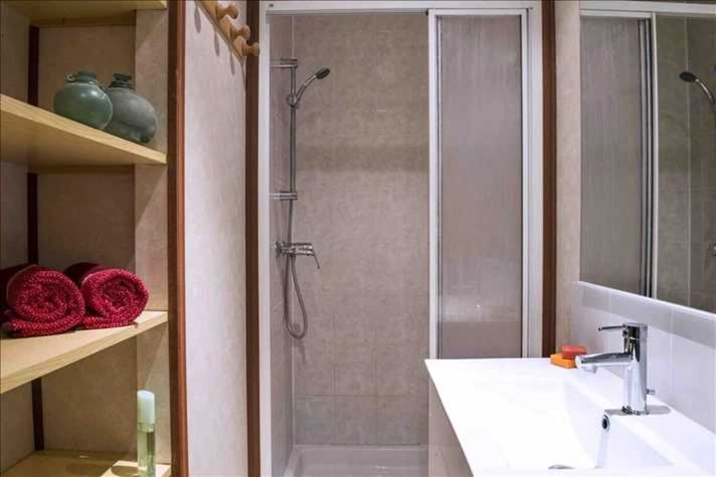 A bathroom with a shower, a sink, and shelves with towels and vases.