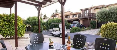 An outdoor patio with a table set for dining, surrounded by chairs, and a pergola overhead.