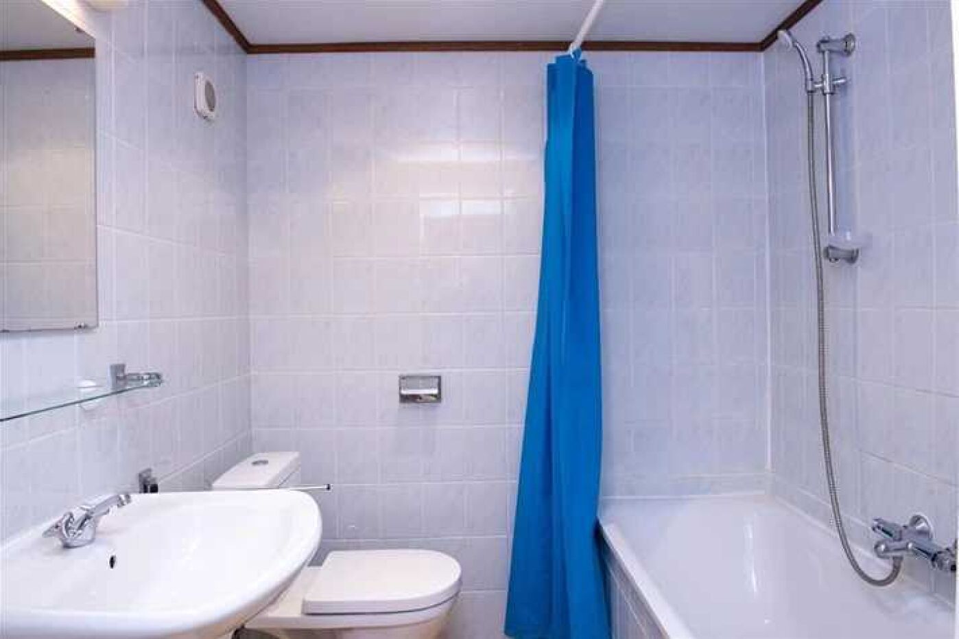 Une salle de bain avec un lavabo, des toilettes et une baignoire blancs, un rideau de douche bleu et des murs carrelés.