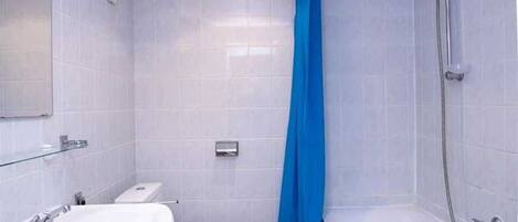 Une salle de bain avec un lavabo, des toilettes et une baignoire blancs, un rideau de douche bleu et des murs carrelés.