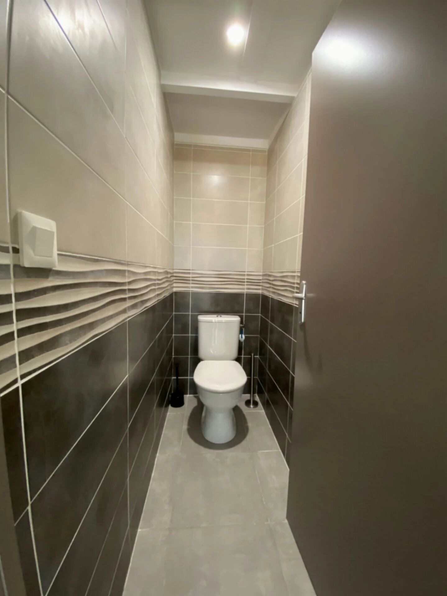 A narrow bathroom with a toilet, a hand dryer, and a wall-mounted light fixture.
