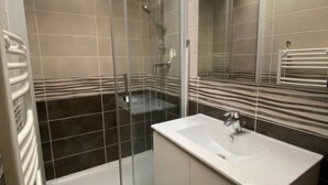 A modern bathroom with a glass-enclosed shower, a white sink, and a large mirror. - ZEcamping piscine couverte dog friendly animations locatif LV BBQ (Léon)
